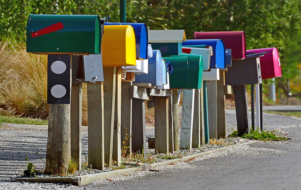 Reihe bunter Briefkästen auf Holzpfosten an einer Landstraße