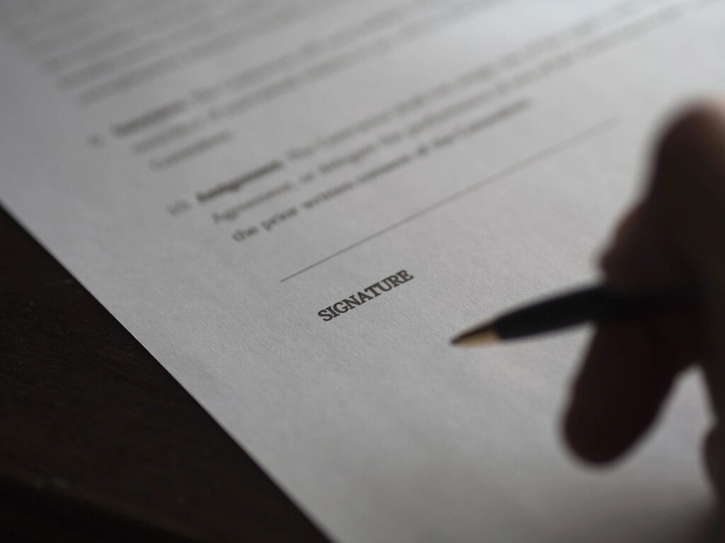 Hand mit Kugelschreiber über der Unterschriftszeile eines Vertrags